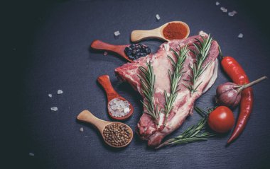 Kaşıklar, biberler, sarımsak, defne yaprağı, acı biber domatesleri ve siyah bir yüzey üzerinde büyük ve taze bir parça et.