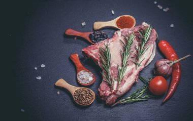 Kaşıklar, biberler, sarımsak, defne yaprağı, acı biber domatesleri ve siyah bir yüzey üzerinde büyük ve taze bir parça et.