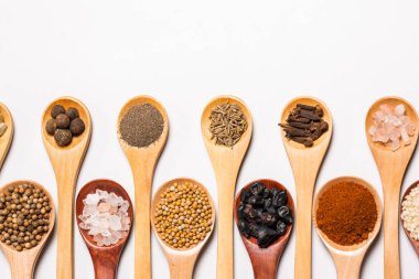 Beyaz arka planda tahta kaşıklardaki baharatlar ve malzemeler