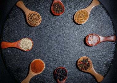 Farklı baharatlar, biberler, kişniş, susam tohumları ve yemek pişirmek için diğerleri siyah arka planda tahta kaşıklarda.