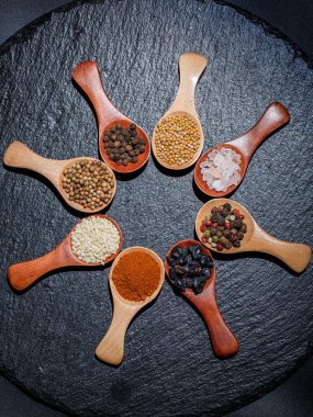 Farklı baharatlar, biberler, kişniş, susam tohumları ve yemek pişirmek için diğerleri siyah arka planda tahta kaşıklarda.
