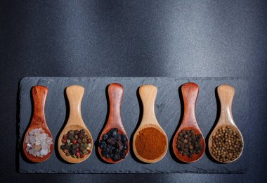 Farklı baharatlar, biberler, kişniş, susam tohumları ve yemek pişirmek için diğerleri siyah arka planda tahta kaşıklarda.