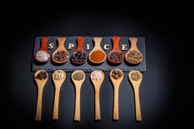 Farklı baharatlar, biberler, kişniş, susam tohumları ve yemek pişirmek için diğerleri siyah arka planda tahta kaşıklarda.