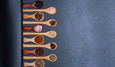 Farklı baharatlar, biberler, kişniş, susam tohumları ve yemek pişirmek için diğerleri siyah arka planda tahta kaşıklarda.