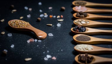 Farklı baharatlar, biberler, kişniş, susam tohumları ve yemek pişirmek için diğerleri siyah arka planda tahta kaşıklarda.