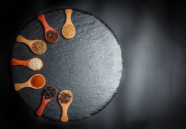 Farklı baharatlar, biberler, kişniş, susam tohumları ve yemek pişirmek için diğerleri siyah arka planda tahta kaşıklarda.