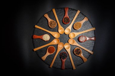 Farklı baharatlar, biberler, kişniş, susam tohumları ve yemek pişirmek için diğerleri siyah arka planda tahta kaşıklarda.