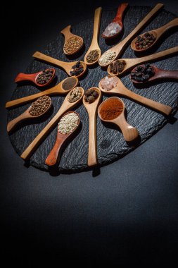 Farklı baharatlar, biberler, kişniş, susam tohumları ve yemek pişirmek için diğerleri siyah arka planda tahta kaşıklarda.