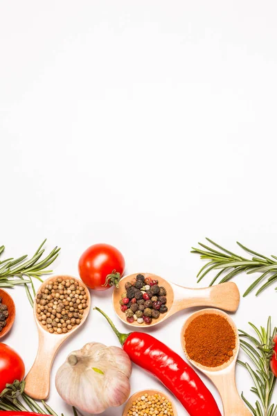 Different spices and ingredients in wooden spoons, different vegetables, hot chili peppers, coriander, garlic, bay leaf for cooking on a white background