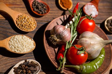 Ahşap kaşıklardaki farklı baharatlar ve pişirmek için farklı malzemeler, kiraz domatesleri, sarımsak, kişniş ve kırmızı biber.