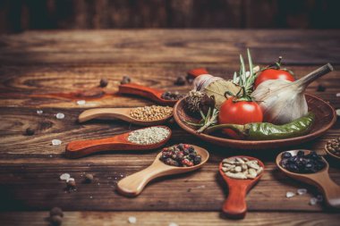Ahşap kaşıklardaki farklı baharatlar ve pişirmek için farklı malzemeler, kiraz domatesleri, sarımsak, kişniş ve kırmızı biber.