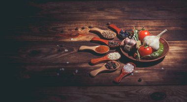 Ahşap kaşıklardaki farklı baharatlar ve pişirmek için farklı malzemeler, kiraz domatesleri, sarımsak, kişniş ve kırmızı biber.