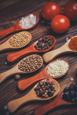 Ahşap kaşıklardaki farklı baharatlar ve pişirmek için farklı malzemeler, kiraz domatesleri, sarımsak, kişniş ve kırmızı biber.