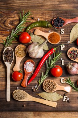 Ahşap kaşıklardaki farklı baharatlar ve pişirmek için farklı malzemeler, kiraz domatesleri, sarımsak, kişniş ve kırmızı biber.