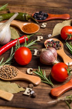 Ahşap kaşıklardaki farklı baharatlar ve pişirmek için farklı malzemeler, kiraz domatesleri, sarımsak, kişniş ve kırmızı biber.