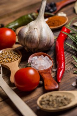 Ahşap kaşıklardaki farklı baharatlar ve pişirmek için farklı malzemeler, kiraz domatesleri, sarımsak, kişniş ve kırmızı biber.