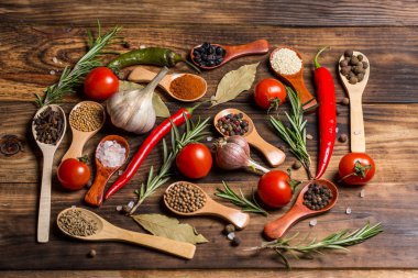 Ahşap kaşıklardaki farklı baharatlar ve pişirmek için farklı malzemeler, kiraz domatesleri, sarımsak, kişniş ve kırmızı biber.