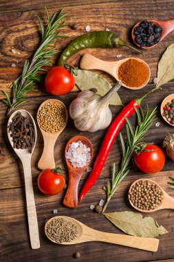 Ahşap kaşıklardaki farklı baharatlar ve pişirmek için farklı malzemeler, kiraz domatesleri, sarımsak, kişniş ve kırmızı biber.