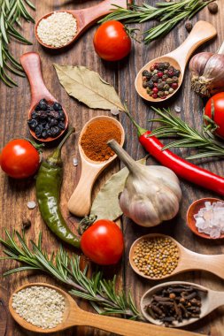 Ahşap kaşıklardaki farklı baharatlar ve pişirmek için farklı malzemeler, kiraz domatesleri, sarımsak, kişniş ve kırmızı biber.