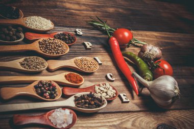 Ahşap kaşıklardaki farklı baharatlar ve pişirmek için farklı malzemeler, kiraz domatesleri, sarımsak, kişniş ve kırmızı biber.