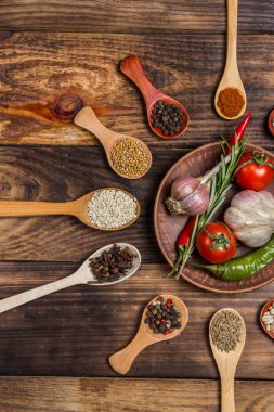 Ahşap kaşıklardaki farklı baharatlar ve pişirmek için farklı malzemeler, kiraz domatesleri, sarımsak, kişniş ve kırmızı biber.