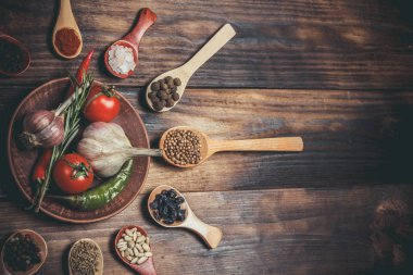 Ahşap kaşıklardaki farklı baharatlar ve pişirmek için farklı malzemeler, kiraz domatesleri, sarımsak, kişniş ve kırmızı biber.