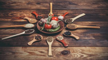 Ahşap kaşıklardaki farklı baharatlar ve pişirmek için farklı malzemeler, kiraz domatesleri, sarımsak, kişniş ve kırmızı biber.