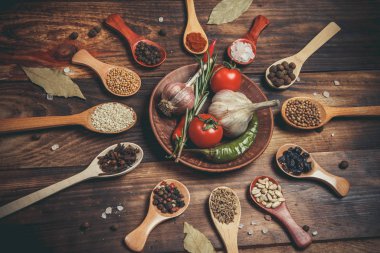 Ahşap kaşıklardaki farklı baharatlar ve pişirmek için farklı malzemeler, kiraz domatesleri, sarımsak, kişniş ve kırmızı biber.