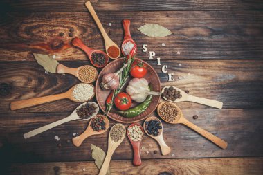 Ahşap kaşıklardaki farklı baharatlar ve pişirmek için farklı malzemeler, kiraz domatesleri, sarımsak, kişniş ve kırmızı biber.