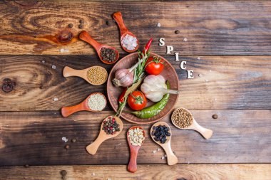 Ahşap kaşıklardaki farklı baharatlar ve pişirmek için farklı malzemeler, kiraz domatesleri, sarımsak, kişniş ve kırmızı biber.