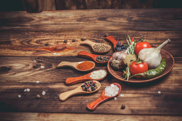 Различные специи в деревянных ложках и различные ингредиенты для приготовления пищи, помидоры черри, чеснок, кориандр и красный перец
