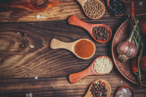 Different spices in wooden spoons and different ingredients for cooking, cherry tomatoes, garlic, coriander and red pepper