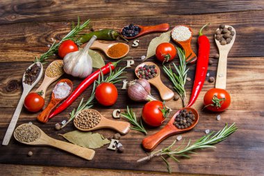 Ahşap kaşıklardaki farklı baharatlar ve pişirmek için farklı malzemeler, kiraz domatesleri, sarımsak, kişniş ve kırmızı biber.