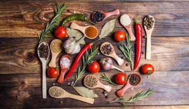 Ahşap kaşıklardaki farklı baharatlar ve pişirmek için farklı malzemeler, kiraz domatesleri, sarımsak, kişniş ve kırmızı biber.