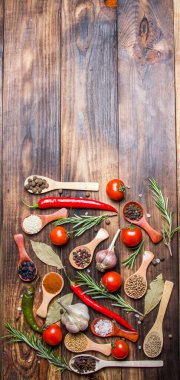 Ahşap kaşıklardaki farklı baharatlar ve pişirmek için farklı malzemeler, kiraz domatesleri, sarımsak, kişniş ve kırmızı biber.