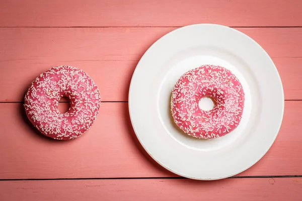 Tasty pink donut on a pink wooden background