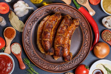 Izgara sosis, sebze, acı biber ve siyah arka planda çeşitli baharatlar.