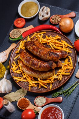 Izgara sosis, sebze, acı biber ve siyah arka planda çeşitli baharatlar.
