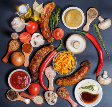 Izgara sosis, sebze, acı biber ve siyah arka planda çeşitli baharatlar.