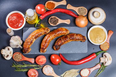 Izgara sosis, sebze, acı biber ve siyah arka planda çeşitli baharatlar.