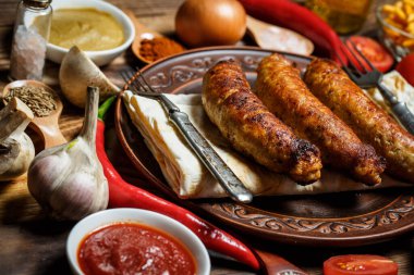 Izgara sosis, taze sebze, ahşap bir masada malzemeler ve baharatlar.