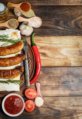 Izgara sosis, taze sebze, ahşap bir masada malzemeler ve baharatlar.