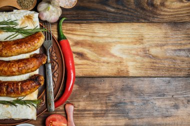 Izgara sosis, taze sebze, ahşap bir masada malzemeler ve baharatlar.