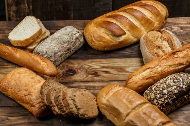 Farklı somun ekmeği ve rulo ekmeği tahtadan bir masa üzerinde un ve buğdayla.