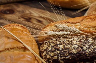 Farklı somun ekmeği ve rulo ekmeği tahtadan bir masa üzerinde un ve buğdayla.