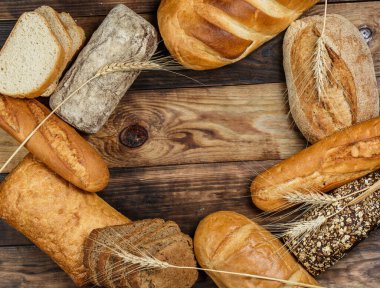 Farklı somun ekmeği ve rulo ekmeği tahtadan bir masa üzerinde un ve buğdayla.