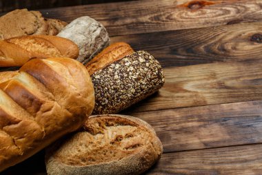 Farklı somun ekmeği ve rulo ekmeği tahtadan bir masa üzerinde un ve buğdayla.