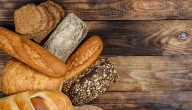 Farklı somun ekmeği ve rulo ekmeği tahtadan bir masa üzerinde un ve buğdayla.