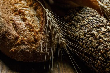 Farklı somun ekmeği ve rulo ekmeği tahtadan bir masa üzerinde un ve buğdayla.