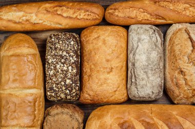 Farklı somun ekmeği ve rulo ekmeği tahtadan bir masa üzerinde un ve buğdayla.